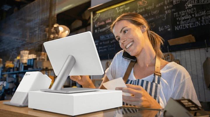 Restaurant employee answering a phone call beside a point-of-sale terminal.